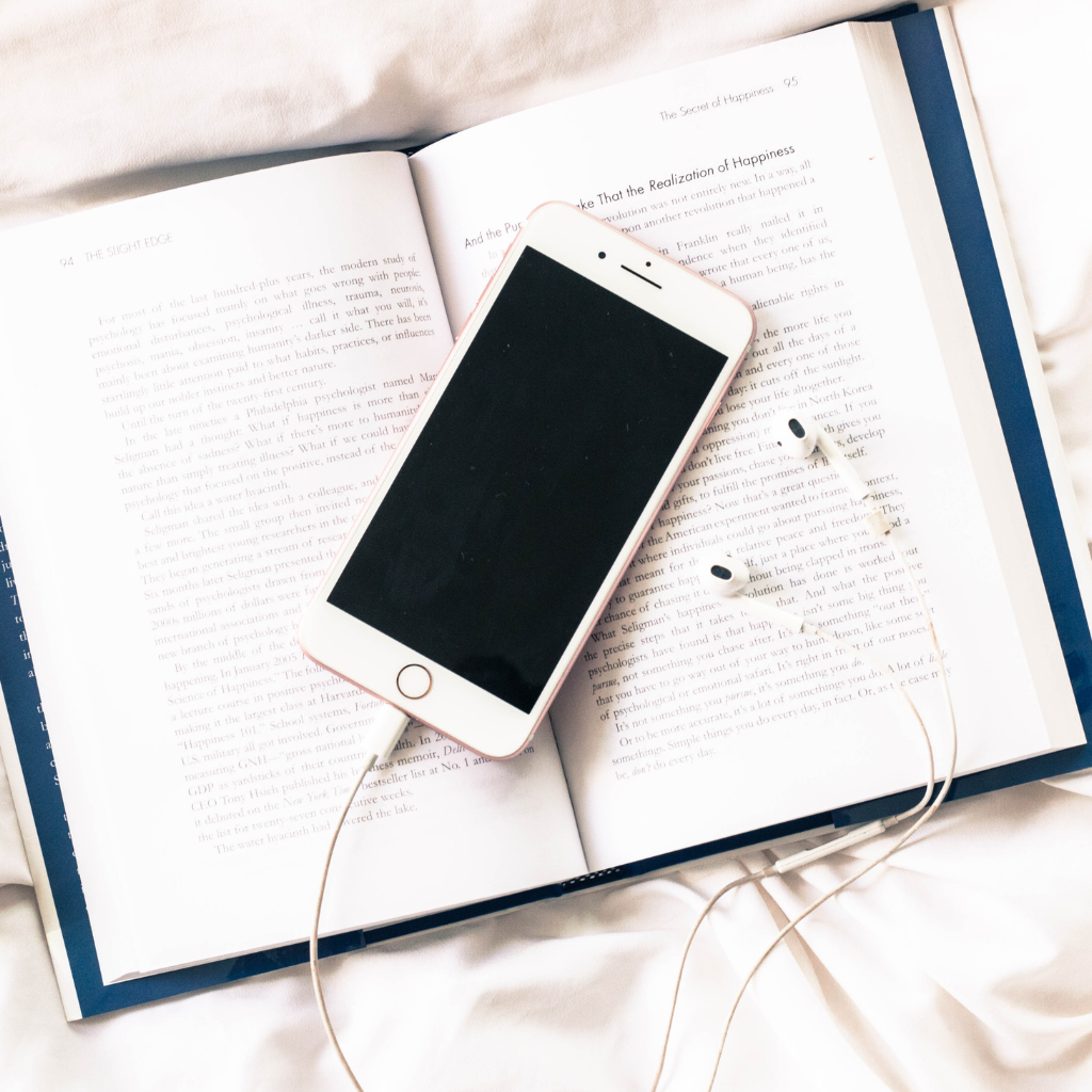 a white cell phone with ear buds on top of a book. Digital Products Devotionals featured